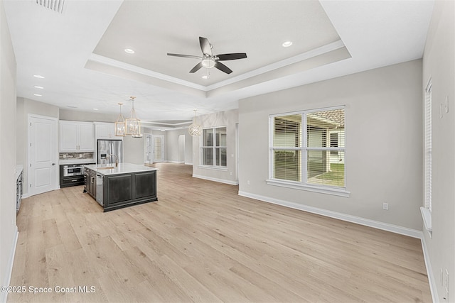 kitchen featuring stainless steel fridge with ice dispenser, decorative light fixtures, a raised ceiling, and a center island with sink