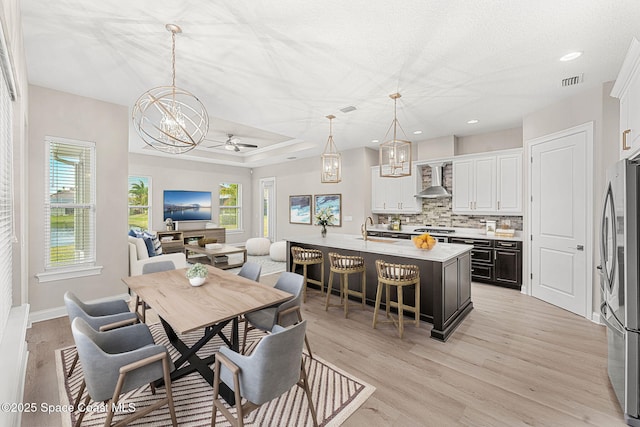 dining space with ceiling fan with notable chandelier, sink, light hardwood / wood-style flooring, and a textured ceiling