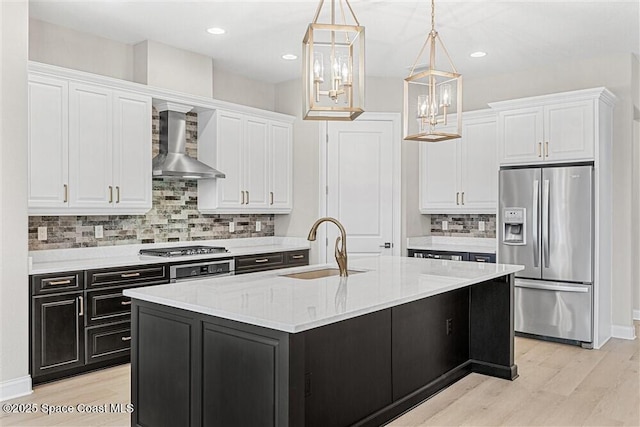 kitchen with appliances with stainless steel finishes, decorative light fixtures, an island with sink, sink, and wall chimney range hood