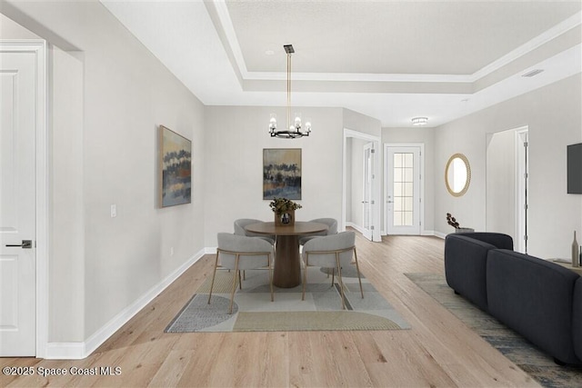 dining space with an inviting chandelier, a tray ceiling, and light hardwood / wood-style floors