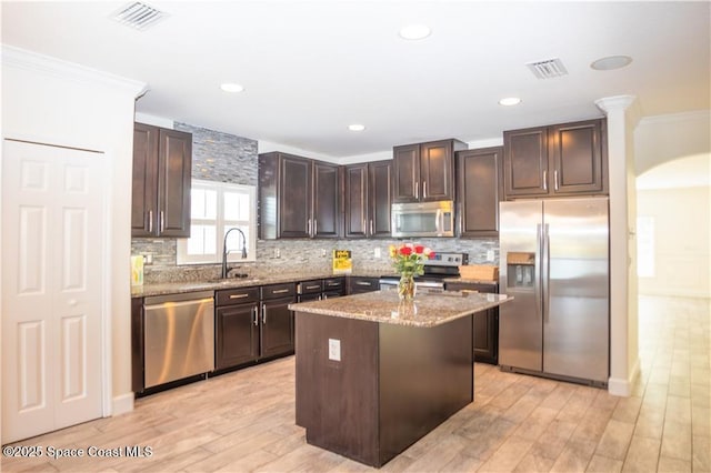 kitchen with sink, appliances with stainless steel finishes, dark brown cabinets, ornamental molding, and a kitchen island