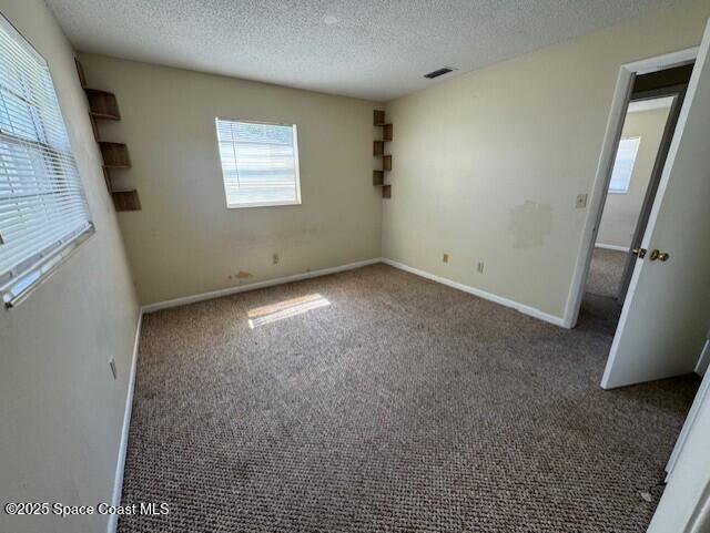 unfurnished bedroom featuring visible vents, baseboards, a textured ceiling, and carpet