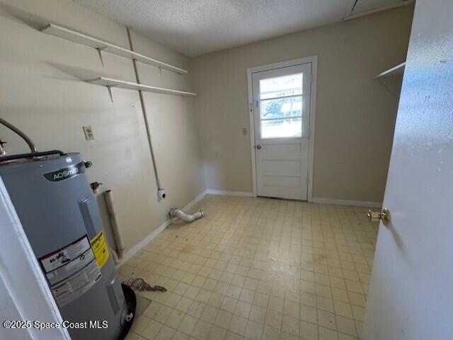 laundry area with electric water heater, a textured ceiling, baseboards, light floors, and laundry area