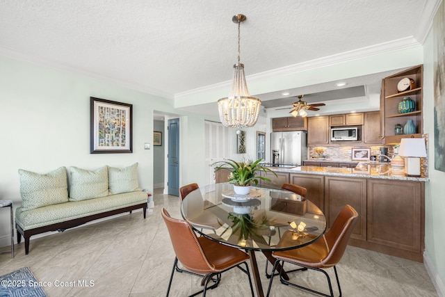 dining space with ceiling fan with notable chandelier, ornamental molding, a raised ceiling, and a textured ceiling