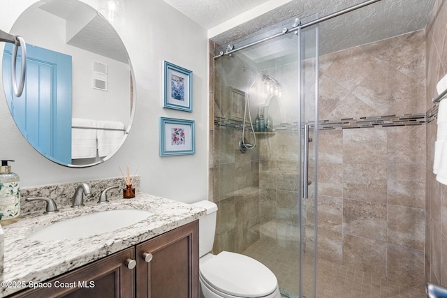 bathroom with a shower with door, vanity, a textured ceiling, and toilet