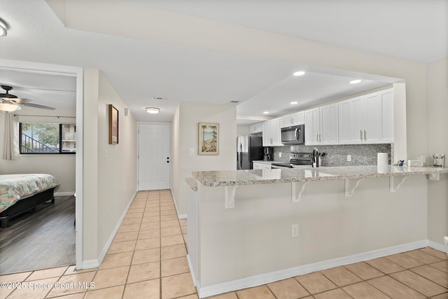 kitchen featuring white cabinetry, tasteful backsplash, light stone counters, kitchen peninsula, and stainless steel appliances