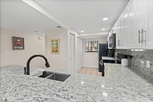 kitchen featuring black electric range oven, sink, light stone counters, white cabinets, and decorative backsplash