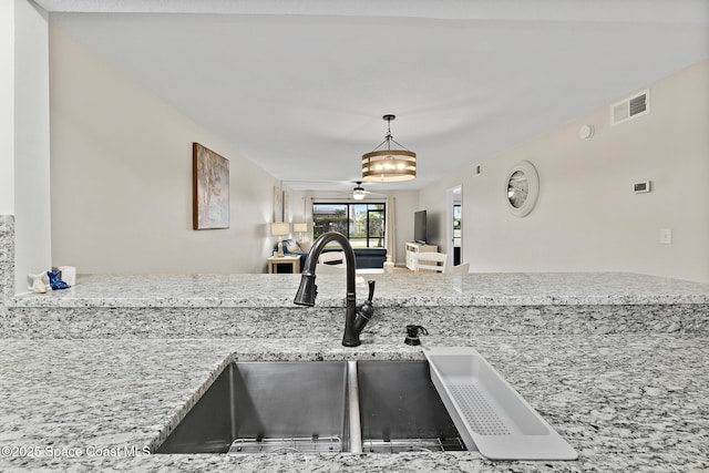 kitchen featuring light stone counters, sink, and decorative light fixtures