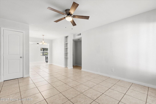 empty room featuring built in shelves, ceiling fan with notable chandelier, and light tile patterned floors