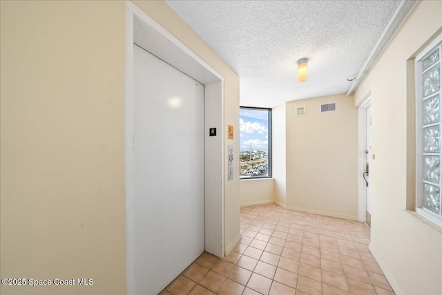 hallway featuring elevator, a textured ceiling, and light tile patterned floors