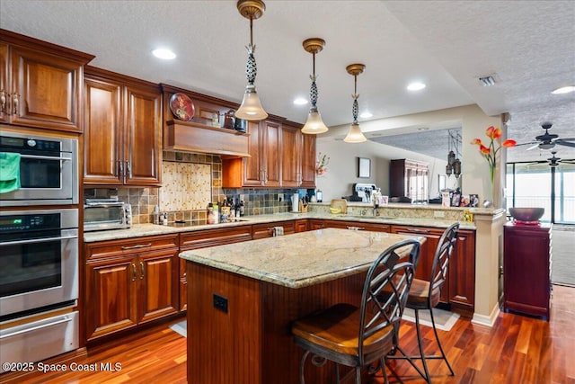 kitchen featuring hanging light fixtures, a kitchen island, black electric stovetop, a kitchen bar, and kitchen peninsula