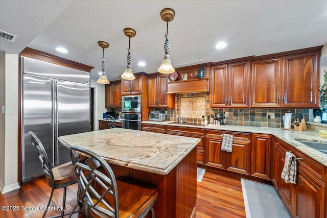 kitchen featuring appliances with stainless steel finishes, a kitchen island, light hardwood / wood-style floors, a kitchen bar, and decorative light fixtures