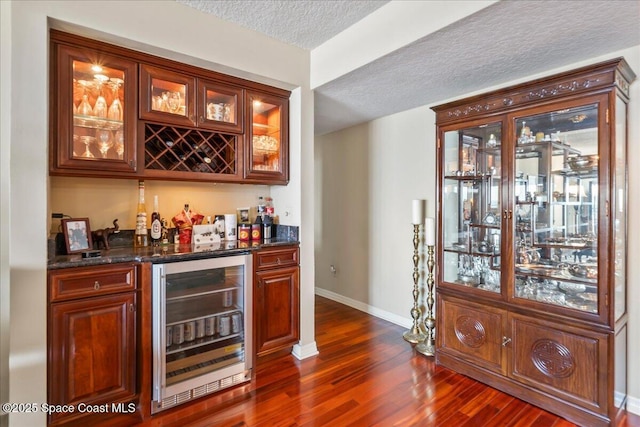 bar featuring wine cooler, dark stone counters, dark wood-type flooring, and a textured ceiling