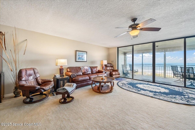 carpeted living room with ceiling fan, floor to ceiling windows, a textured ceiling, and a water view