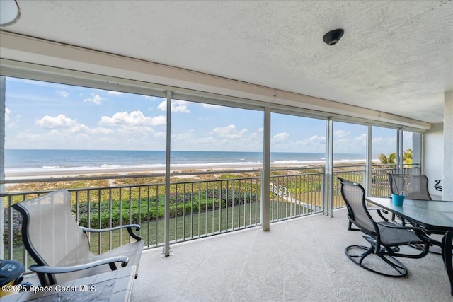 sunroom featuring a beach view and a water view