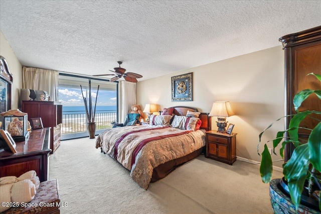 carpeted bedroom featuring a water view, a wall of windows, a textured ceiling, access to outside, and ceiling fan