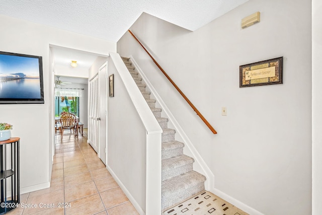 stairway featuring ceiling fan, tile patterned floors, and a textured ceiling