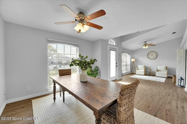 dining room with ceiling fan, vaulted ceiling, a textured ceiling, and light wood-type flooring