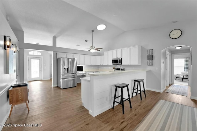 kitchen with a kitchen breakfast bar, kitchen peninsula, hardwood / wood-style flooring, stainless steel appliances, and white cabinets