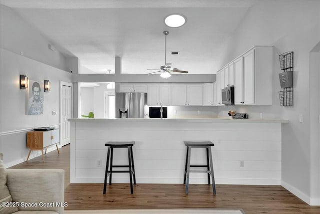 kitchen with dark wood-type flooring, a breakfast bar area, stainless steel appliances, white cabinets, and kitchen peninsula