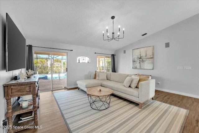 living room with lofted ceiling, a notable chandelier, light hardwood / wood-style flooring, and a textured ceiling