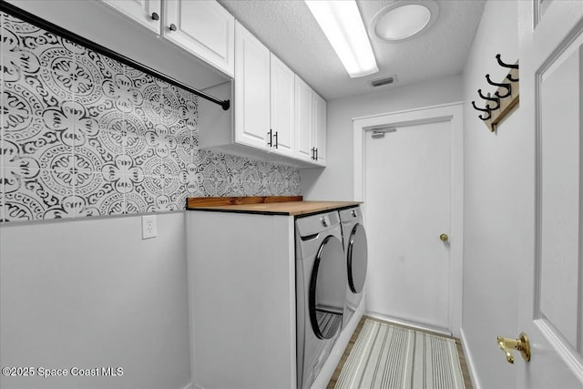 clothes washing area with cabinets, washer and dryer, and a textured ceiling