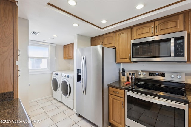 kitchen featuring light tile patterned flooring, appliances with stainless steel finishes, dark stone countertops, a raised ceiling, and washing machine and dryer