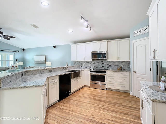 kitchen with appliances with stainless steel finishes, sink, white cabinets, light stone counters, and kitchen peninsula