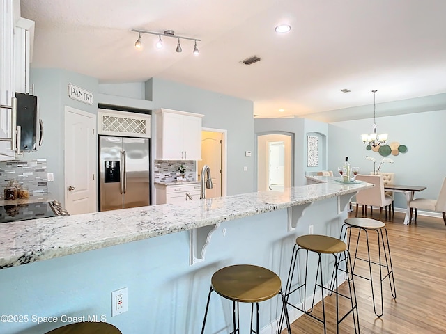 kitchen featuring pendant lighting, appliances with stainless steel finishes, backsplash, light hardwood / wood-style floors, and white cabinets