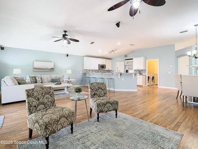 living room with ceiling fan with notable chandelier, lofted ceiling, washer and clothes dryer, and light hardwood / wood-style floors