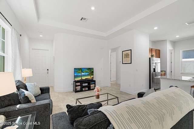 living room featuring a tray ceiling and light tile patterned flooring
