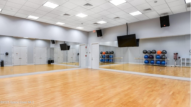 workout area featuring wood-type flooring, a towering ceiling, and a paneled ceiling