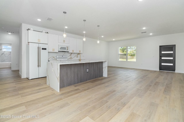 kitchen featuring decorative light fixtures, white cabinets, a large island, light stone counters, and white appliances