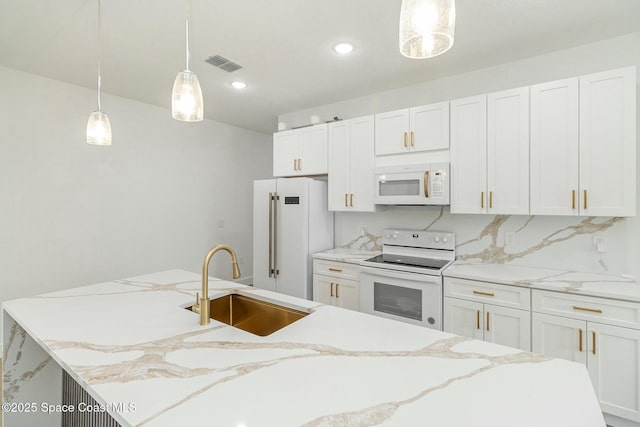 kitchen featuring pendant lighting, sink, white cabinets, a kitchen island with sink, and white appliances