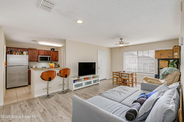 living room with ceiling fan, light hardwood / wood-style floors, and a textured ceiling