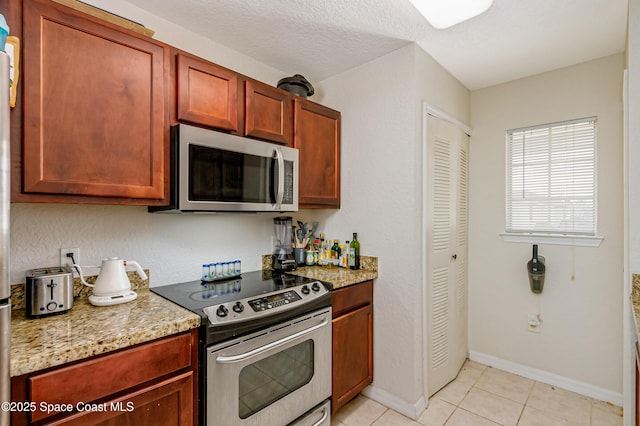 kitchen with light stone counters, light tile patterned flooring, a textured ceiling, and appliances with stainless steel finishes