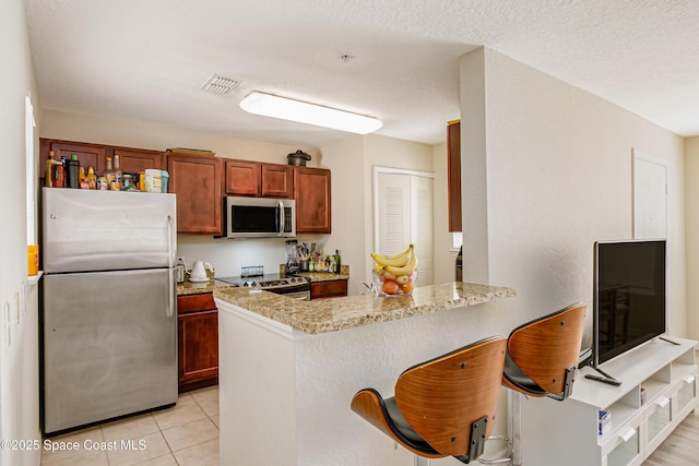 kitchen featuring light tile patterned floors, a breakfast bar, stainless steel appliances, light stone counters, and kitchen peninsula