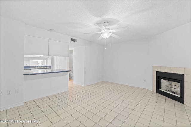 unfurnished living room with sink, a textured ceiling, light tile patterned floors, ceiling fan, and a fireplace