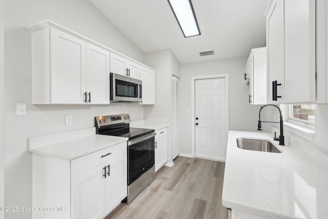 kitchen featuring white cabinetry, lofted ceiling, sink, stainless steel appliances, and light stone countertops