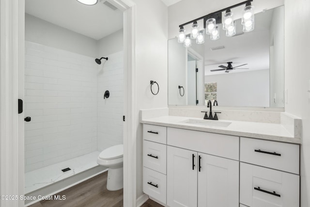 bathroom with hardwood / wood-style flooring, vanity, tiled shower, and toilet