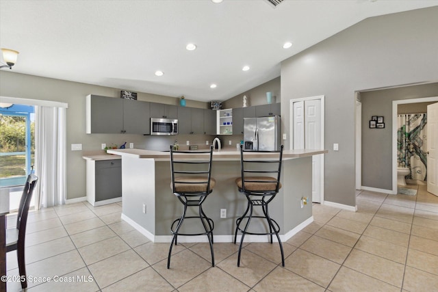 kitchen with stainless steel appliances, vaulted ceiling, gray cabinets, and a kitchen island with sink