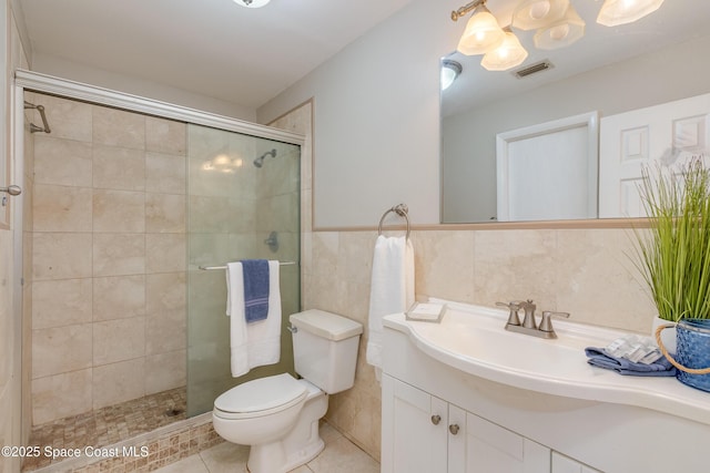 bathroom with tile patterned floors, toilet, a shower with shower door, tile walls, and vanity