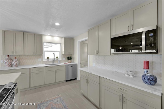 kitchen featuring appliances with stainless steel finishes, sink, decorative backsplash, light stone counters, and a textured ceiling