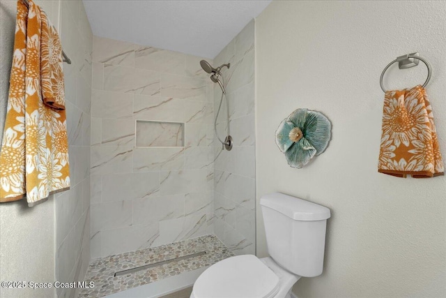 bathroom featuring tiled shower and toilet