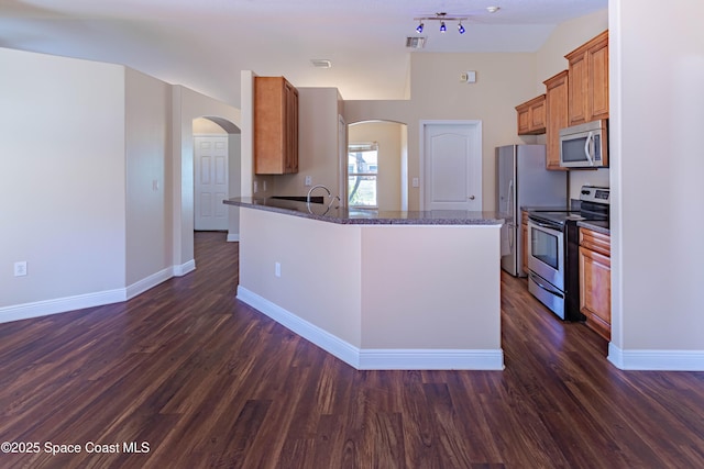 kitchen with dark stone countertops, dark hardwood / wood-style floors, stainless steel appliances, and kitchen peninsula