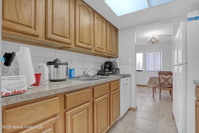 kitchen featuring light tile patterned flooring, sink, tasteful backsplash, a skylight, and white fridge