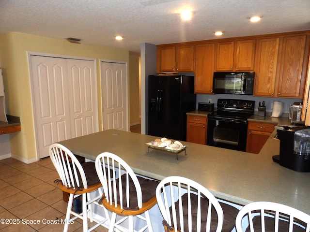 kitchen with a breakfast bar area, light tile patterned floors, kitchen peninsula, and black appliances