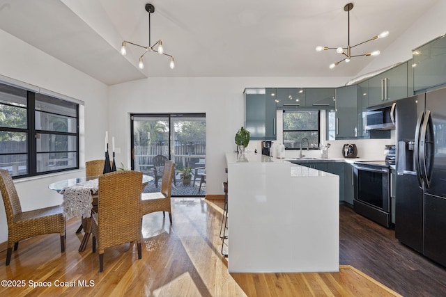 kitchen featuring pendant lighting, dark wood-type flooring, stainless steel appliances, a notable chandelier, and vaulted ceiling