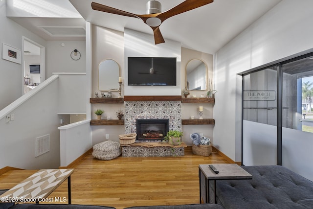 living room with wood-type flooring, a stone fireplace, and lofted ceiling