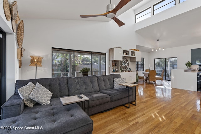 living room featuring ceiling fan, plenty of natural light, a towering ceiling, and light wood-type flooring